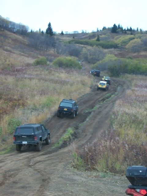 1979 Ford Bronco - Multiple SUVs navigate a challenging dirt track through a hilly, brush-covered landscape.