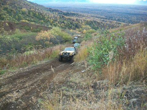 1979 Ford Bronco - A convoy of off-road vehicles navigates a steep, muddy trail through a wooded, mountainous landscape.