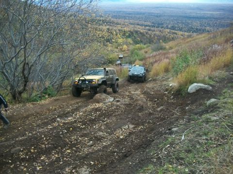 1979 Ford Bronco - Off-road vehicles traverse a challenging dirt path through a wooded, hilly landscape.