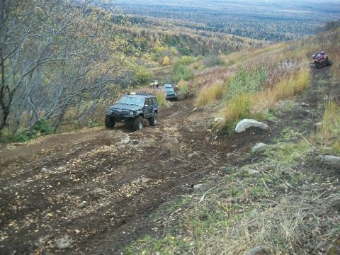 1979 Ford Bronco - Off-road vehicles navigate a challenging, muddy trail through a forest during autumn.