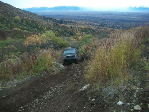 1979 Ford Bronco - Two Jeep Cherokee XJs navigate a challenging off-road trail through a wooded mountain area.