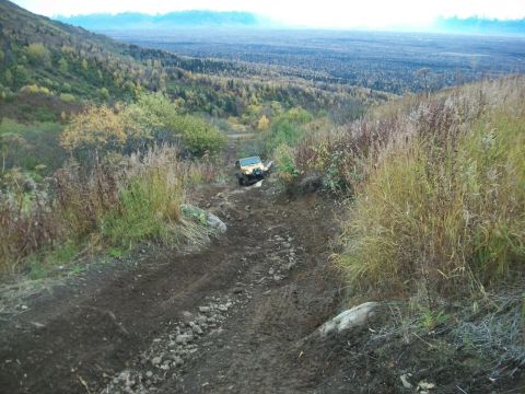1979 Ford Bronco - A yellow SUV navigates a challenging off-road trail through a wooded, mountainous landscape.