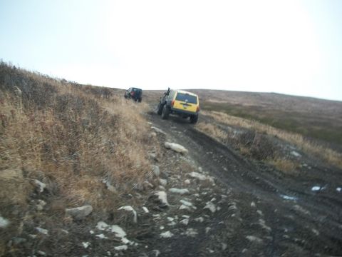 1979 Ford Bronco - Two SUVs navigate a challenging off-road trail on a grassy, rocky hillside.