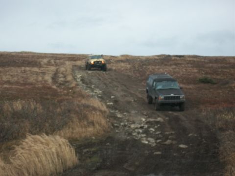 1979 Ford Bronco - Two SUVs navigate a rough dirt road through a barren, grassy terrain.