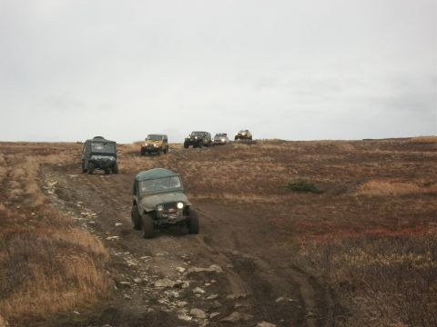1979 Ford Bronco - A convoy of off-road vehicles navigates a challenging, muddy terrain on a cloudy day.