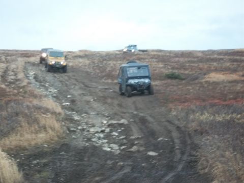 1979 Ford Bronco - A convoy of off-road vehicles makes its way up a challenging dirt track, traversing a desolate, grassy landscape.