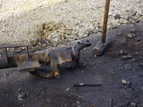 1992 Ford Bronco - A heavily rusted vehicle axle component lies on the ground next to a sledgehammer, suggesting repair or disassembly.