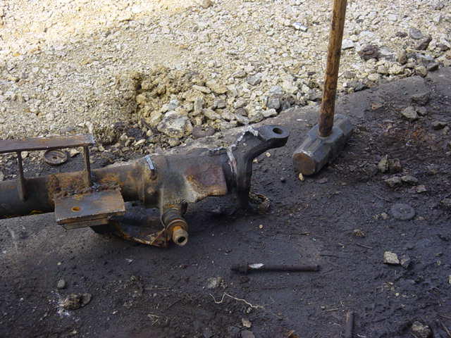 Rusted vehicle axle component with a sledgehammer nearby on dirty ground