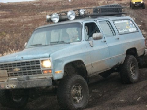 1979 Ford Bronco - This light blue SUV, likely from the 1970s, navigates a muddy off-road course with aftermarket modifications.