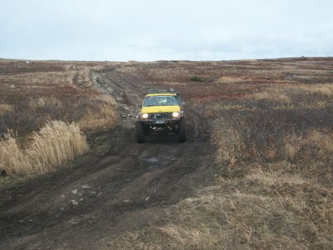 1979 Ford Bronco - Off-road SUV navigates a challenging muddy terrain under an overcast sky.