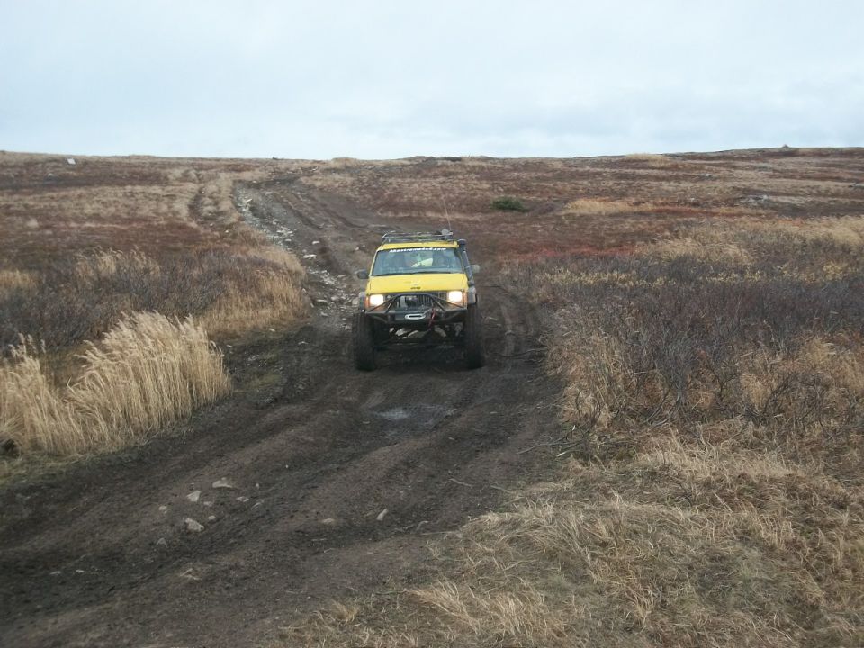 Yellow off-road SUV driving on a muddy, rutted track through a barren landscape