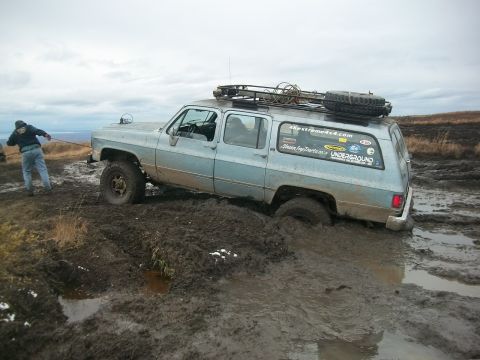 1979 Ford Bronco - A person pulls a light blue SUV out of deep mud with a rope.