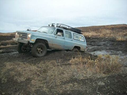 1979 Ford Bronco - This Chevrolet Suburban is stuck in a muddy field, its front-left wheel deeply embedded in the mire.
