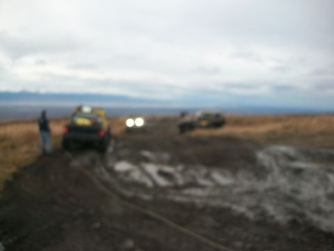 1979 Ford Bronco - Several off-road vehicles are seen traversing a challenging muddy path, with one vehicle in the foreground and others further ahead.
