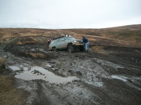 1979 Ford Bronco - A person is winching a light blue SUV out of a muddy, off-road terrain.