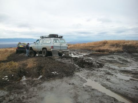 1979 Ford Bronco - Two SUVs are stuck in deep mud on an off-road trail under a cloudy sky.