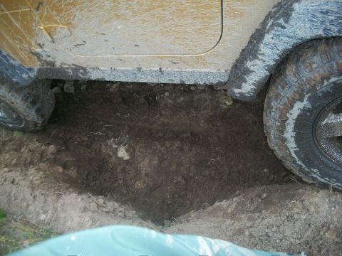 1979 Ford Bronco - An off-road vehicle is stuck in a deep muddy hole, with its tires partially submerged in the dirt.