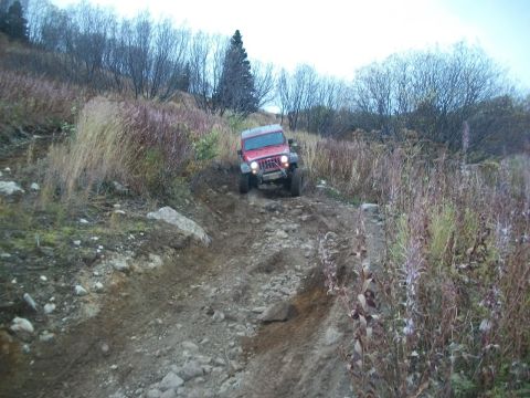 1979 Ford Bronco - A red Jeep Wrangler navigates a challenging off-road path on a hillside.
