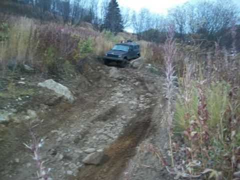1979 Ford Bronco - A dark SUV navigates a challenging off-road path with steep inclines and loose terrain.