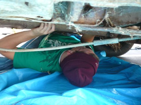 1988 Ford Bronco - A person works on the undercarriage of a vehicle, with a blue tarp spread out below.