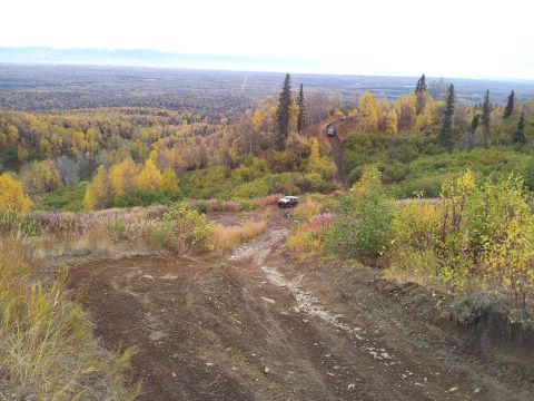 1990 Chevrolet Suburban - Two SUVs navigate a challenging dirt path amidst a colorful autumn forest landscape.