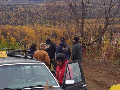 1990 Chevrolet Suburban - A group of people stand around SUVs in a wooded area during autumn.