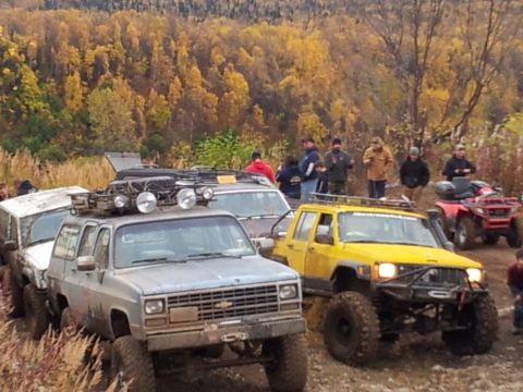 1990 Chevrolet Suburban - A group of off-road vehicles are parked on a trail during autumn, with people gathered around.