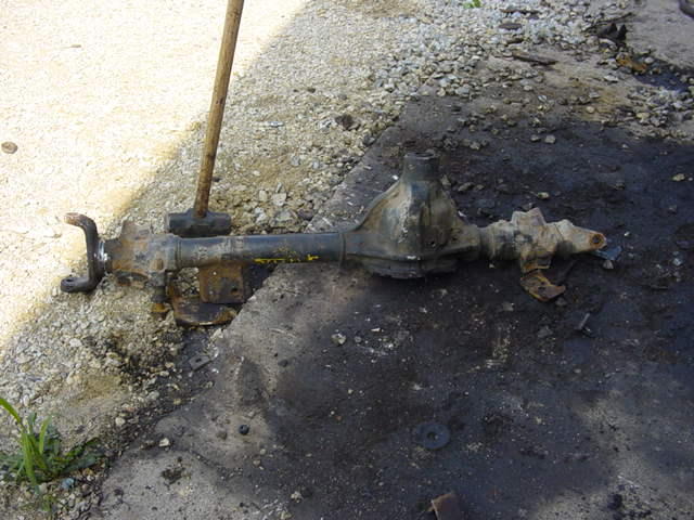 Rusty front axle assembly with a wooden handle resting on it