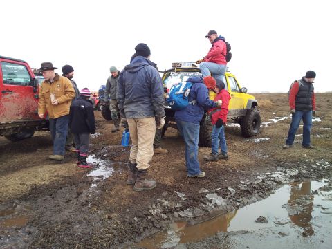 1990 Chevrolet Suburban - A group of people stand around a yellow Jeep Wrangler in a muddy, off-road environment.