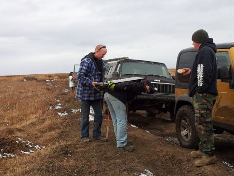 1990 Chevrolet Suburban - People gathered around a Jeep Cherokee in a muddy, outdoor setting with other vehicles present.