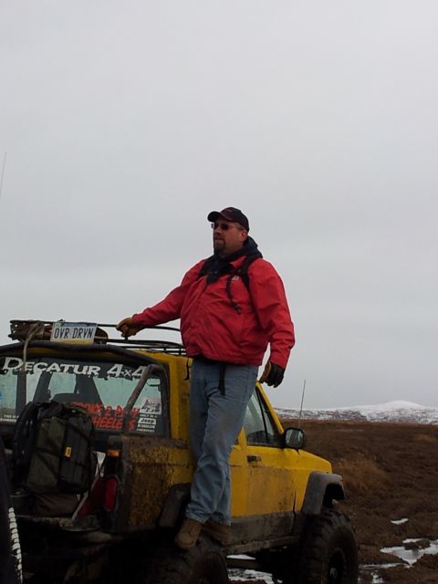 1990 Chevrolet Suburban - A man stands on the rear of a mud-covered yellow off-road vehicle, with 'DECATUR 4x4' visible on the side.