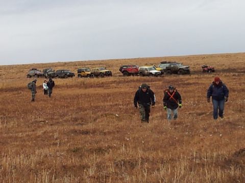 1990 Chevrolet Suburban - Several off-road vehicles are parked on a grassy hill under an overcast sky, with a group of people walking towards the viewer.