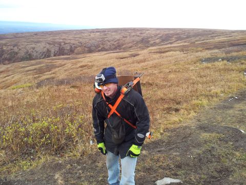1990 Chevrolet Suburban - Man wearing a backpack with a camera mounted on his hat, standing in a desolate landscape.