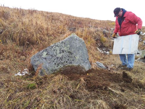 1990 Chevrolet Suburban - A person stands in a dry, grassy area next to a large boulder, holding a flat object.