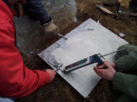 1990 Chevrolet Suburban - Two individuals are shown applying sealant to a metal plate with a caulking gun and putty knives.