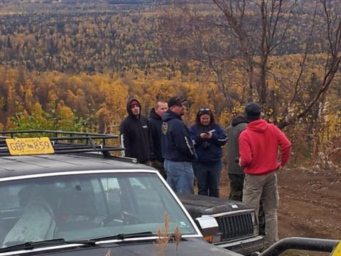 1990 Chevrolet Suburban - A group of people stand around vehicles in a wooded area with autumn foliage.