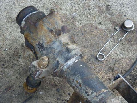 1992 Ford Bronco - A close-up of a heavily rusted axle component, with a safety pin lying nearby on the ground.