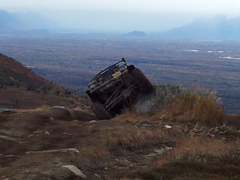 1990 Chevrolet Suburban - An off-road vehicle navigates a steep, rocky terrain with a vast valley stretching out behind it.