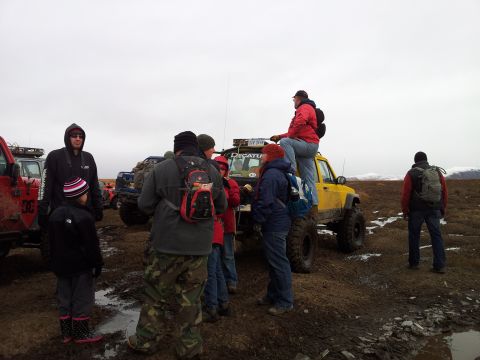 1990 Chevrolet Suburban - A group of people stand around a yellow Jeep in a muddy, outdoor setting.