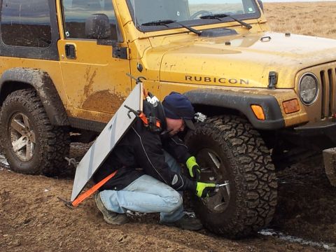 1990 Chevrolet Suburban - Man changes tire on a yellow Jeep Wrangler Rubicon off-road.