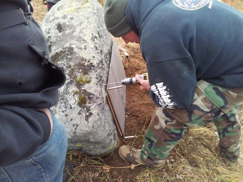 1990 Chevrolet Suburban - A person drills into a large rock while another person watches, with a wooden panel leaning against the rock.