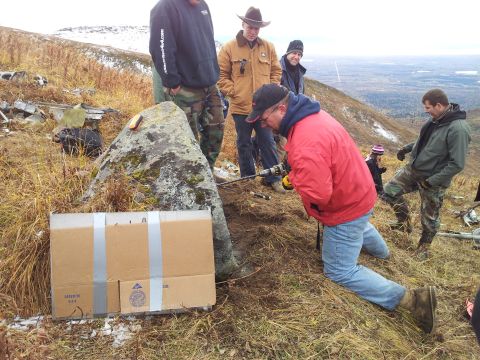 1990 Chevrolet Suburban - People work on a hillside with a rock and a taped box, with a distant view of a valley.