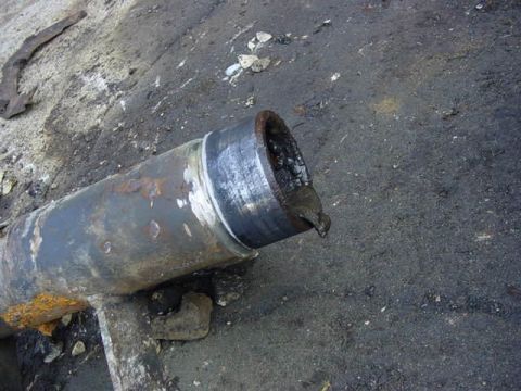 1992 Ford Bronco - A close-up view of a corroded metal pipe, likely a vehicle part, resting on a rough surface.
