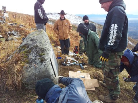 1990 Chevrolet Suburban - A group of individuals are engaged in an activity around a large rock, with tools and equipment laid out on the ground.