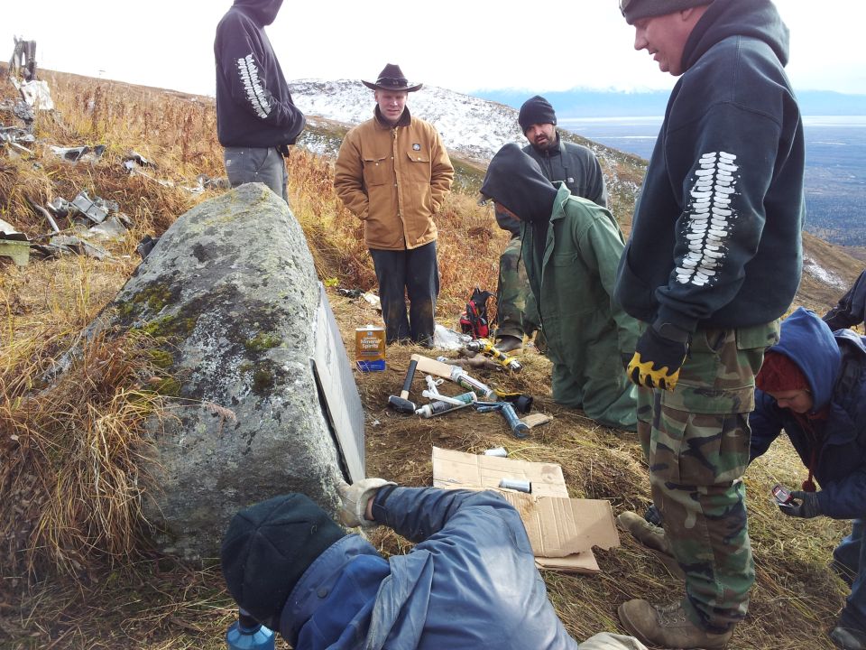 People gathered around a large rock with tools, working on its surface