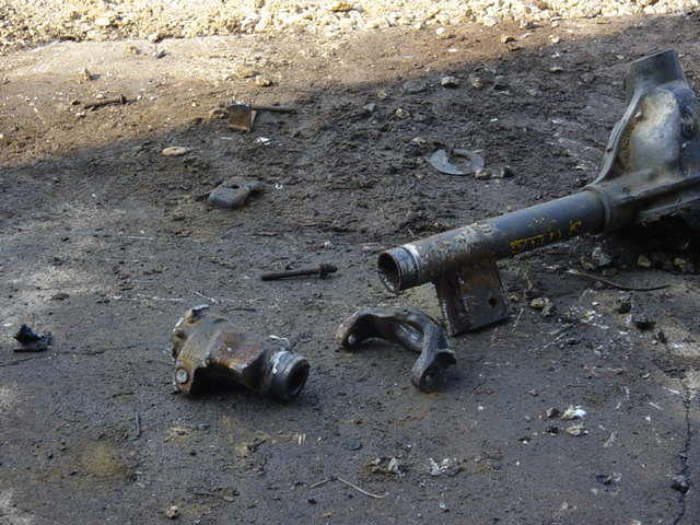 Stripped axle housing tube with cut-off knuckle and steering arm on oily gravel