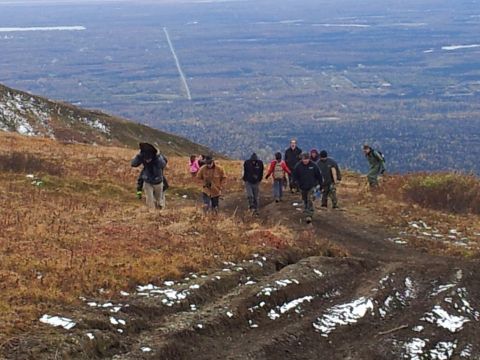 1990 Chevrolet Suburban - A group of hikers makes their way up a challenging trail, with a wide, forested landscape stretching out below.