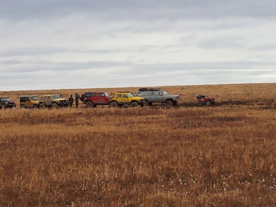 Gray SUV with roof rack and other off-road vehicles in a line on a dry, grassy plain