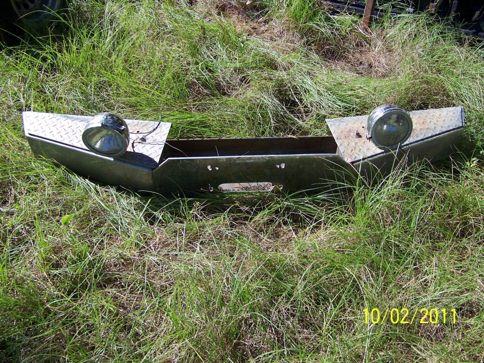 Custom metal bumper with diamond plate accents and two round lights, lying in grass
