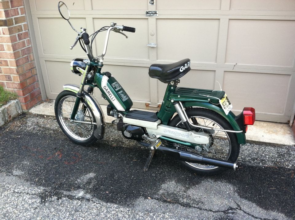 Green and white Garelli moped parked in front of a garage door. Chrome fenders and handlebars